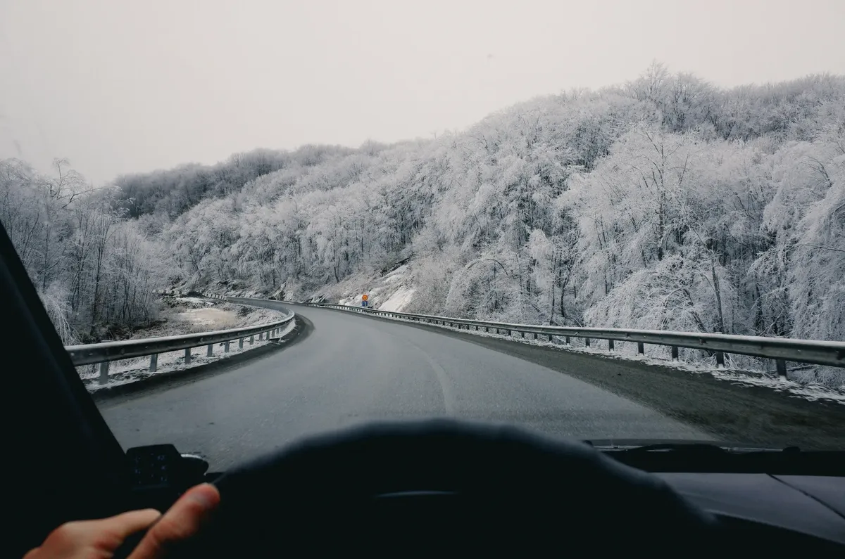 Driving on a winter road with snow-covered trees, view from the car interior.
